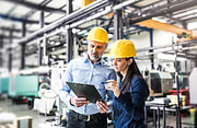 Man and female factory workers look at clipboard